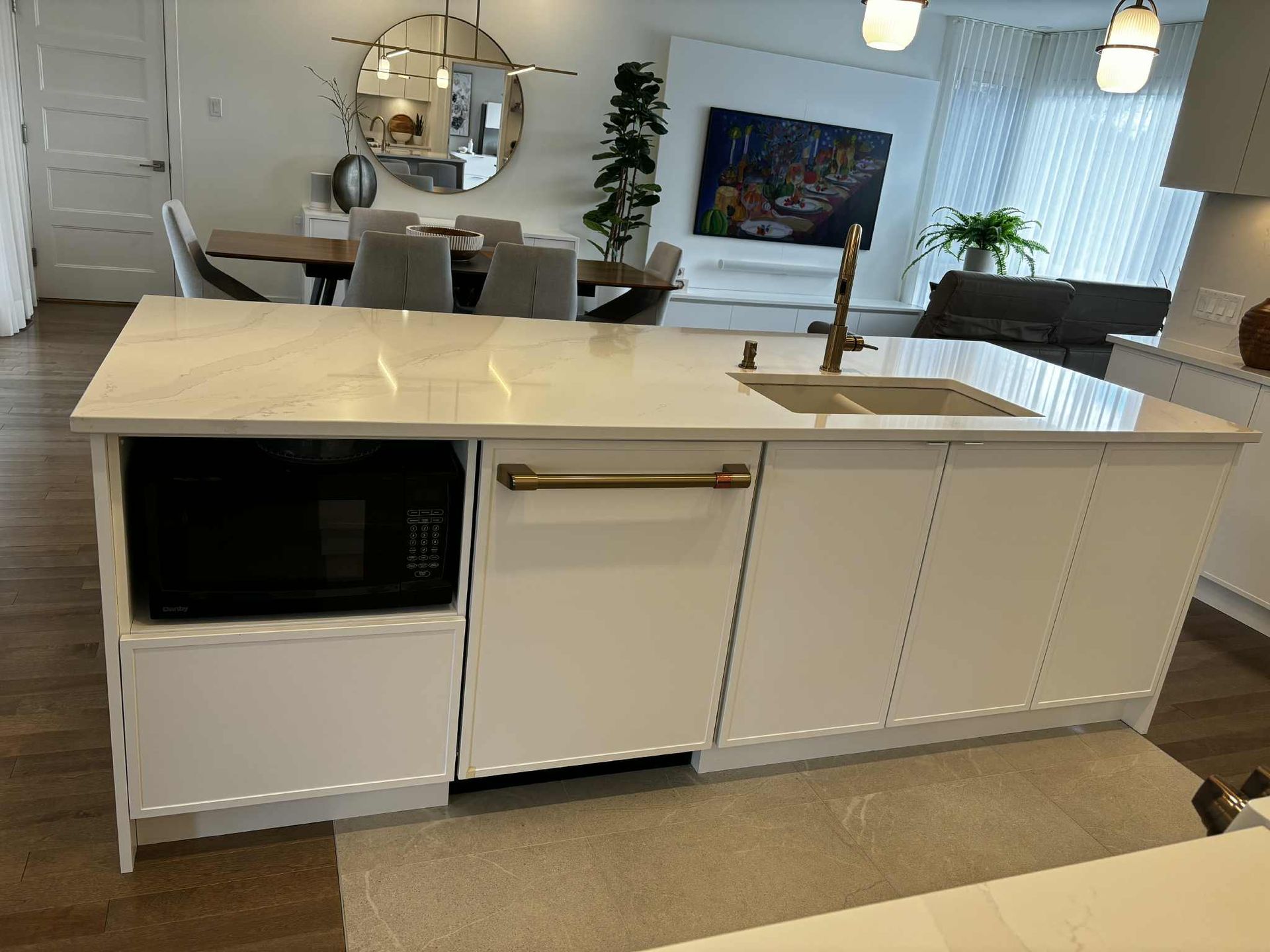 Îlot de cuisine blanc avec comptoir en marbre, micro-ondes, lave-vaisselle et évier.