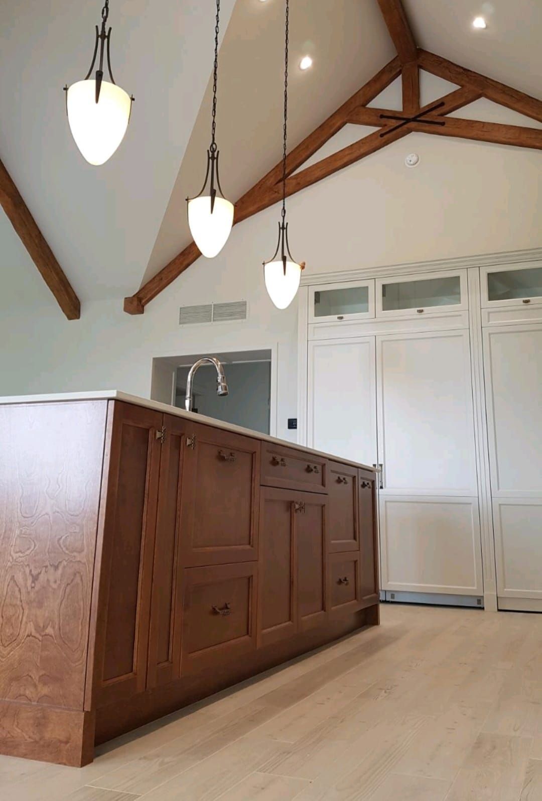 Cuisine avec îlot en bois, trois suspensions lumineuses, placards blancs et poutres apparentes.