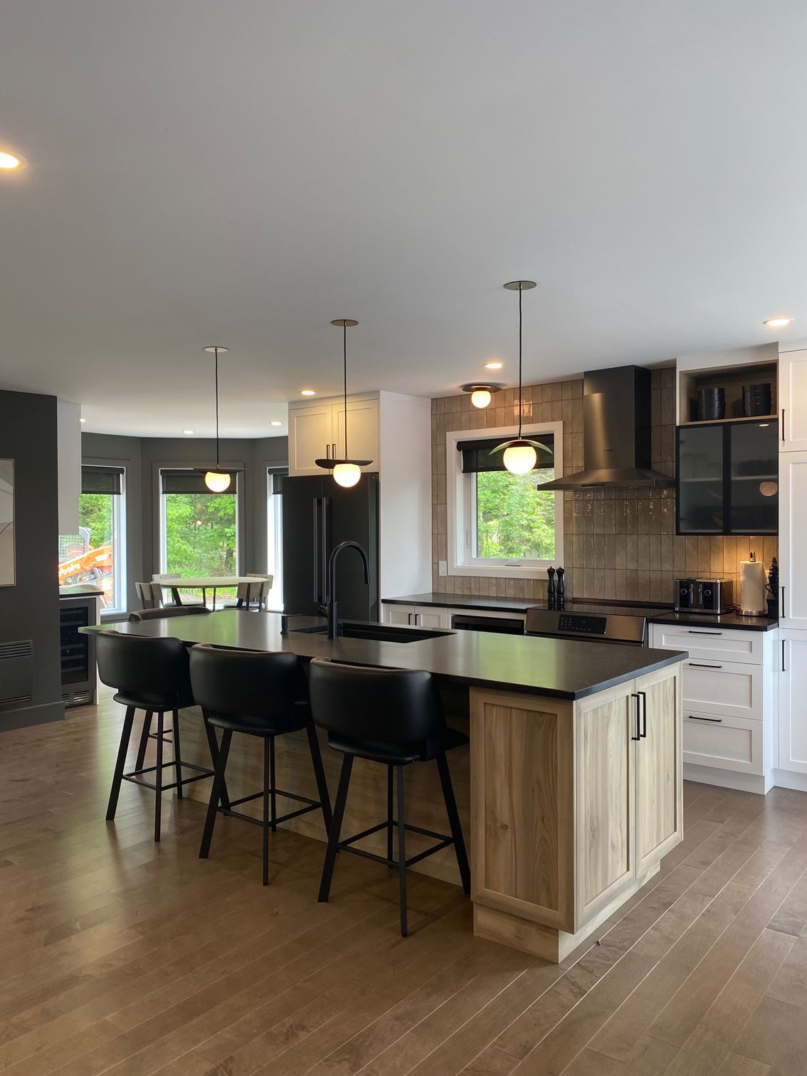 Cuisine moderne avec îlot en bois, tabourets noirs, plans de travail noirs et suspensions lumineuses.