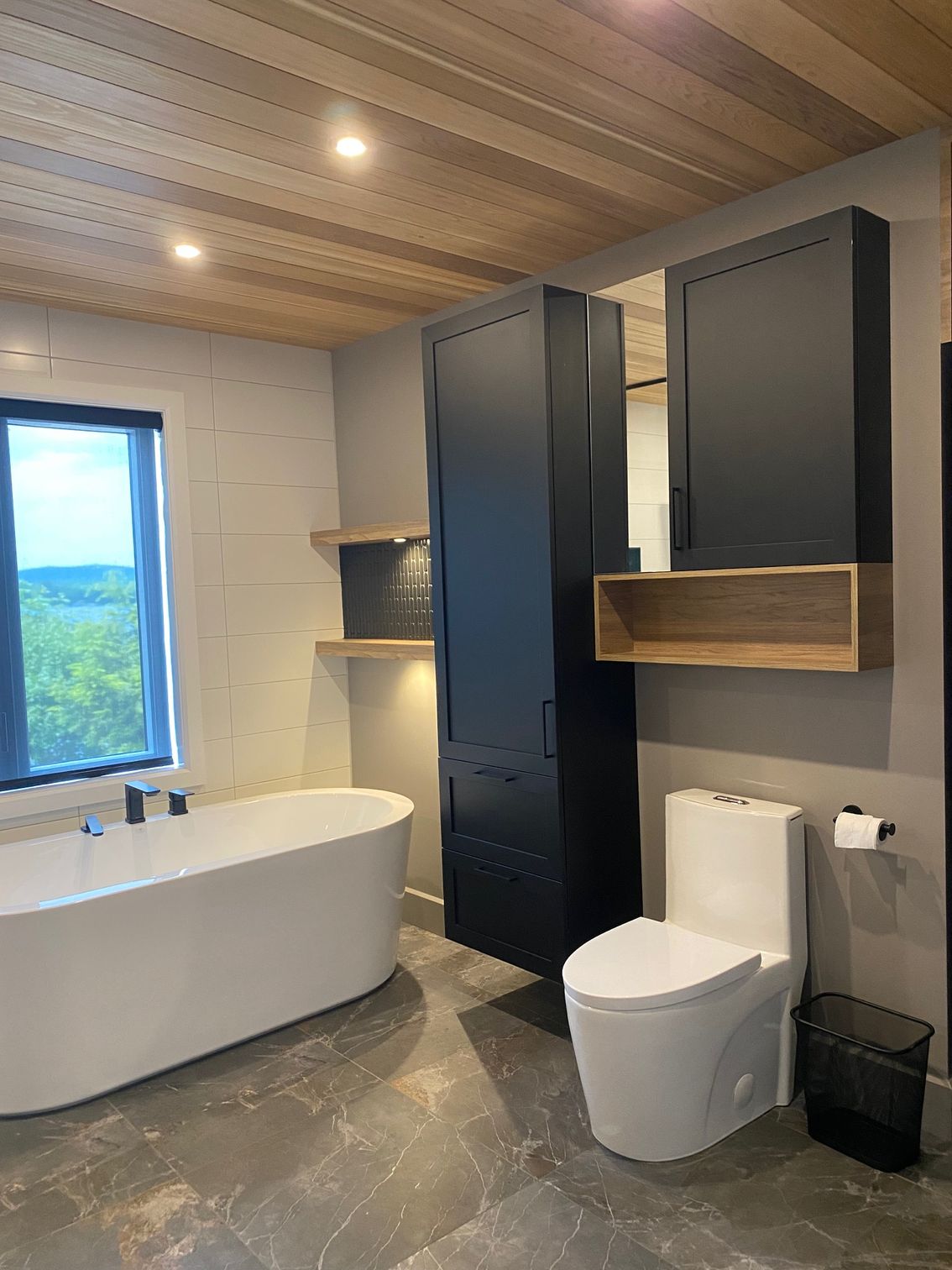 Salle de bains moderne avec baignoire blanche, meubles noirs et plafond en bois.