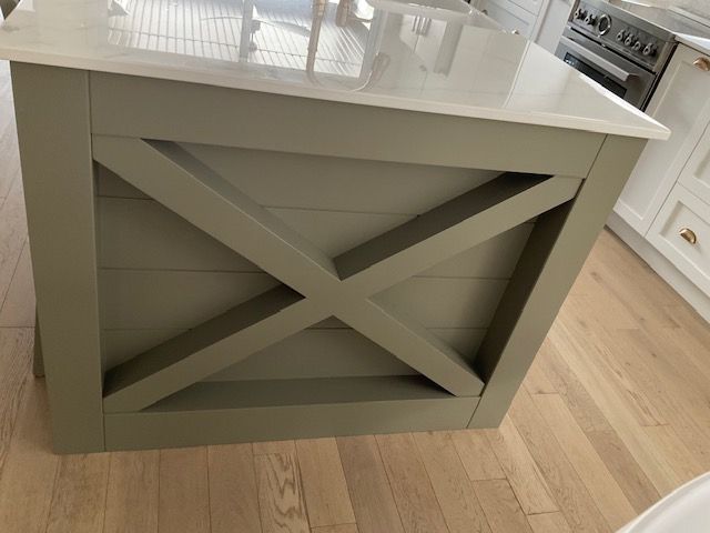 Îlot de cuisine avec placards vert clair, plan de travail blanc et parquet.