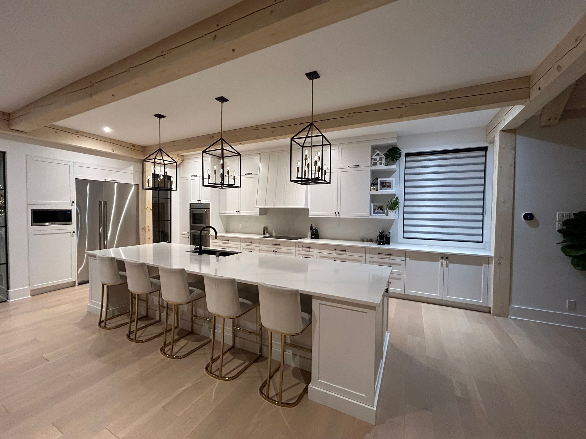 Cuisine blanche moderne avec îlot central, suspensions lumineuses, poutres en bois et tabourets de bar.