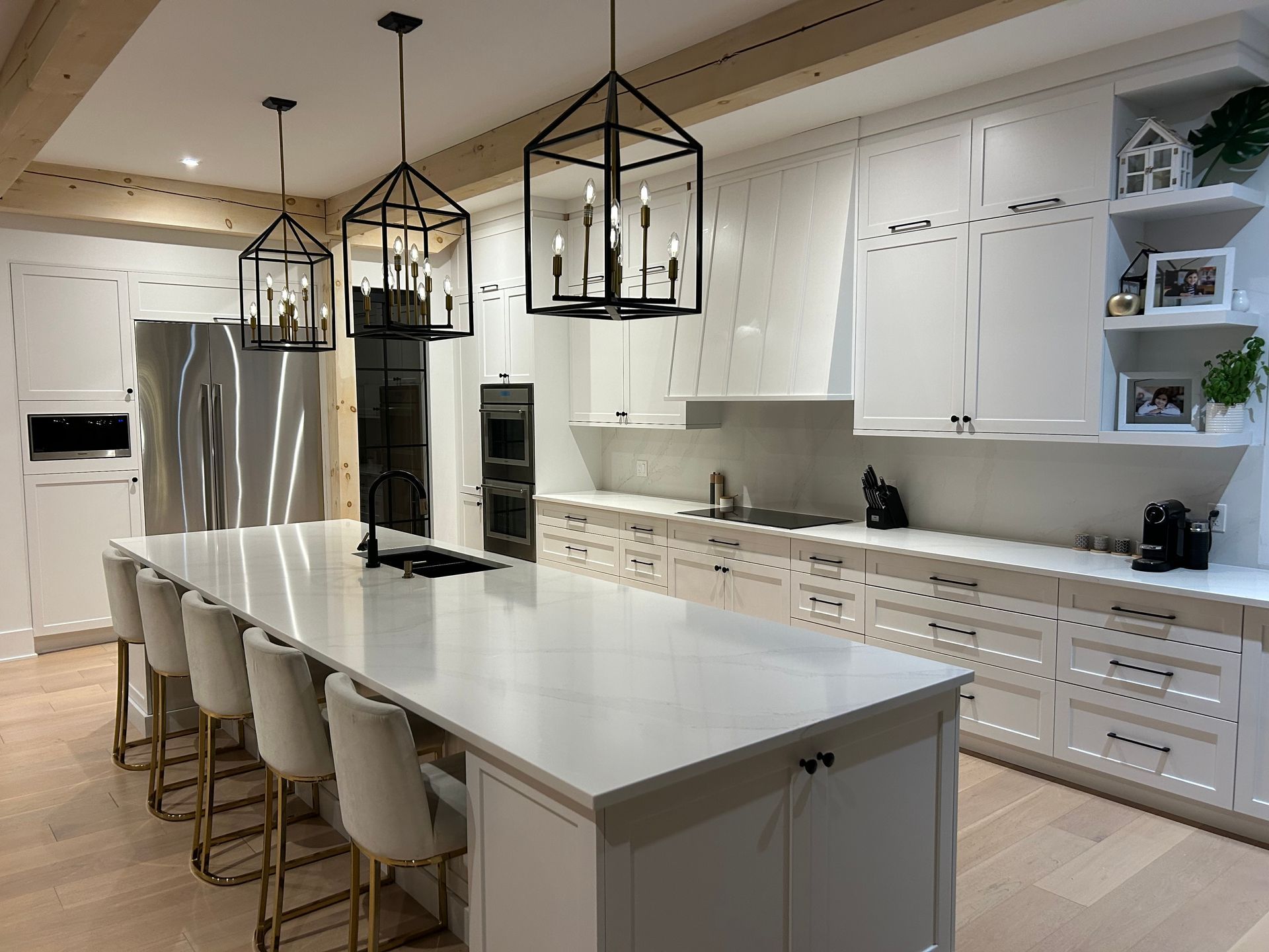Cuisine moderne blanche avec un grand îlot central, des suspensions lumineuses noires et des appareils électroménagers en acier inoxydable.