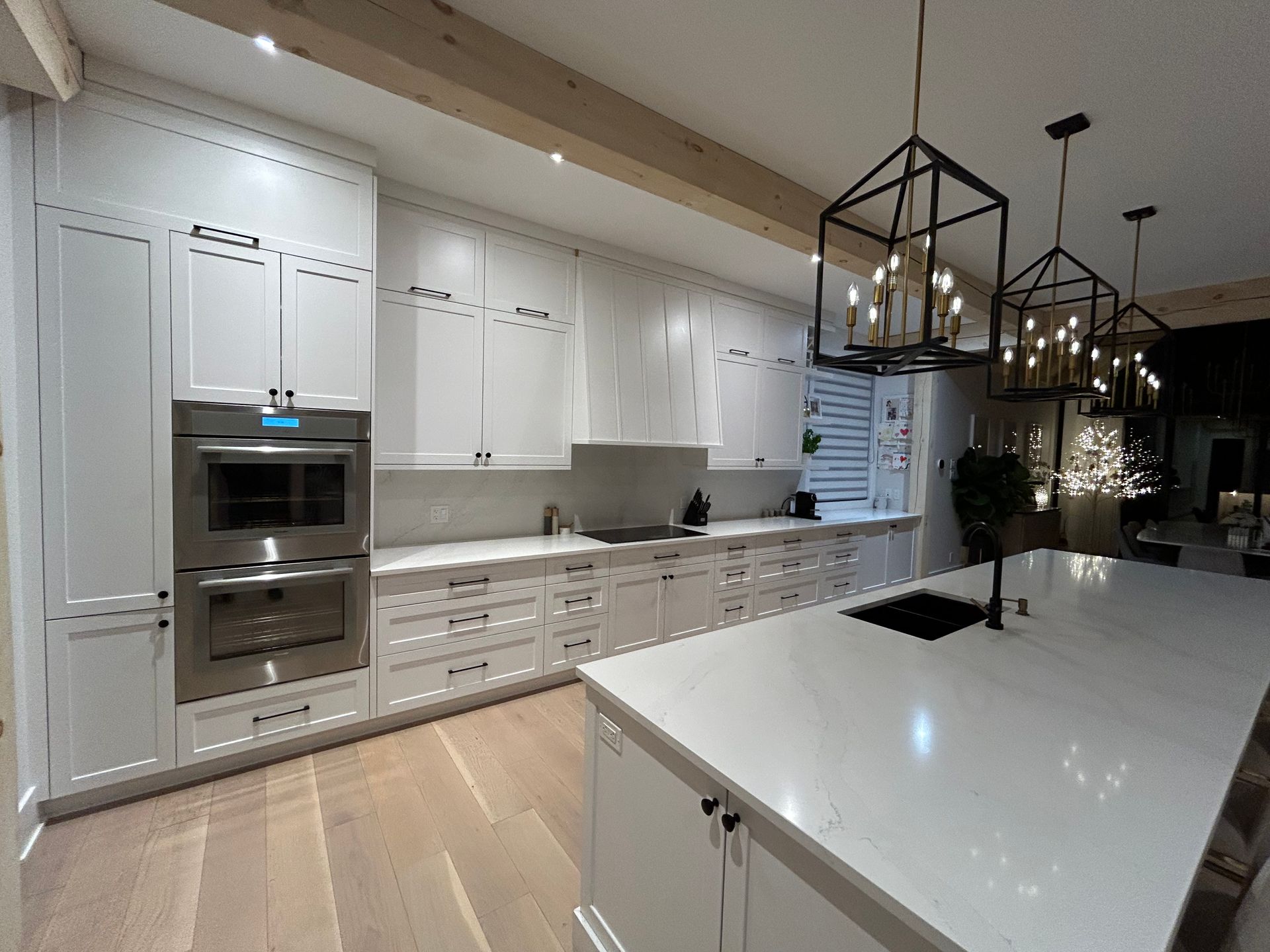 Cuisine moderne blanche avec îlot central, parquet et suspensions lumineuses noires.