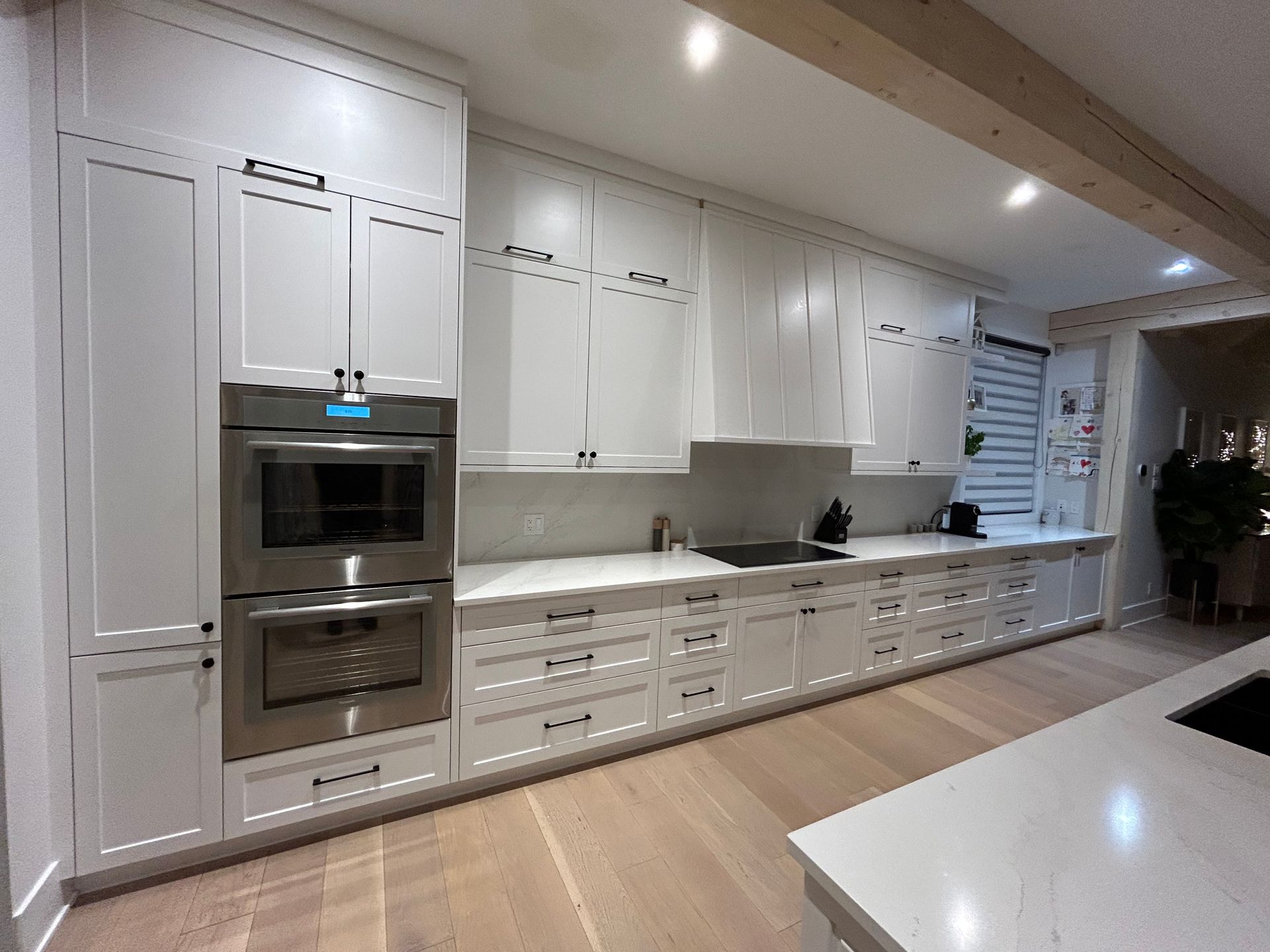 Cuisine blanche avec placards, four encastré et plan de travail blanc. Parquet clair et poutre apparente.