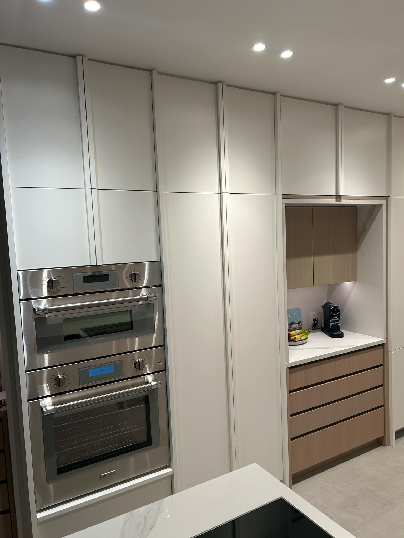 Cuisine avec placards blancs, four en inox et tiroirs en bois clair.