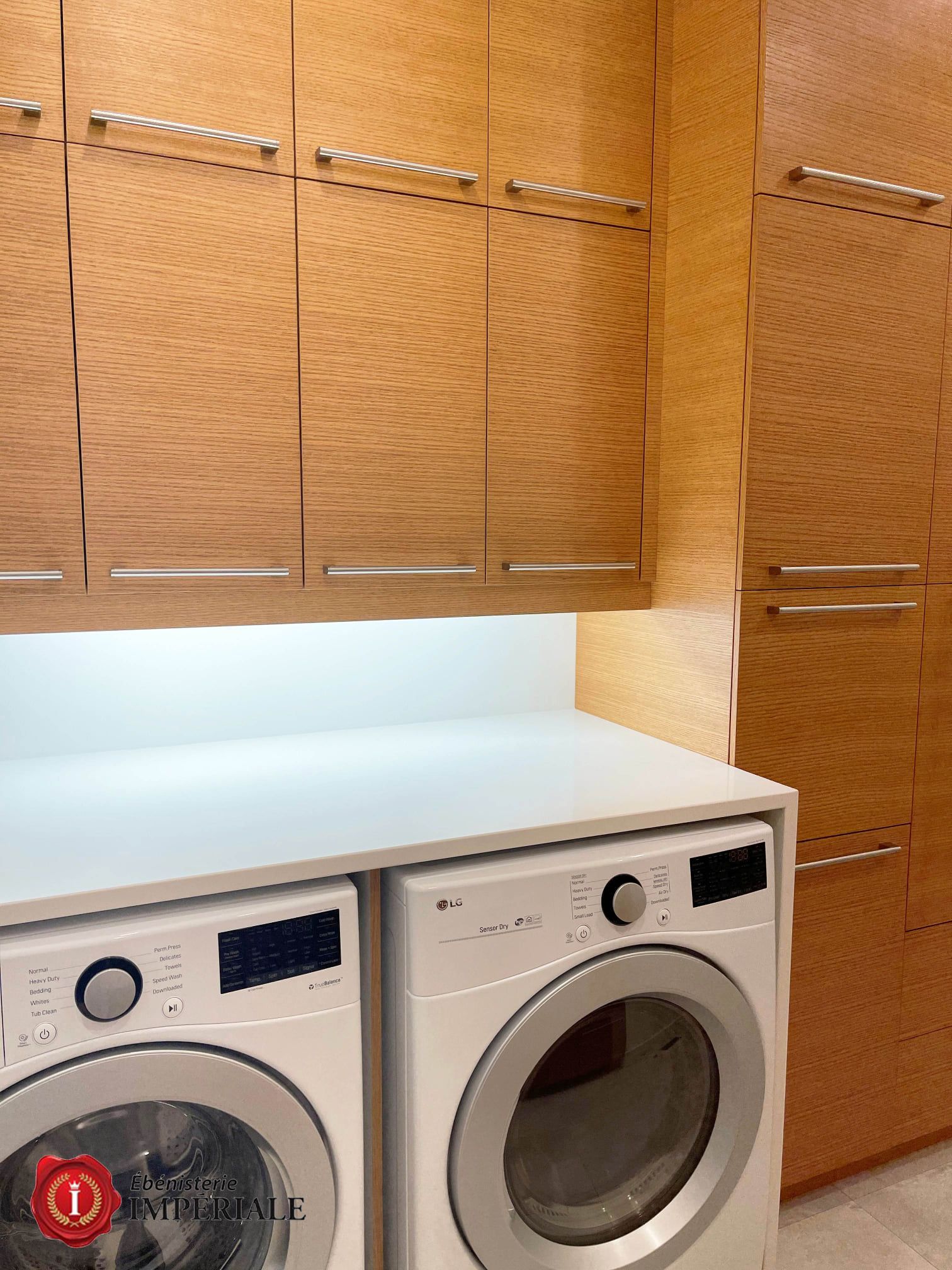 Buanderie avec lave-linge et sèche-linge blancs, placards en bois clair et plan de travail blanc.