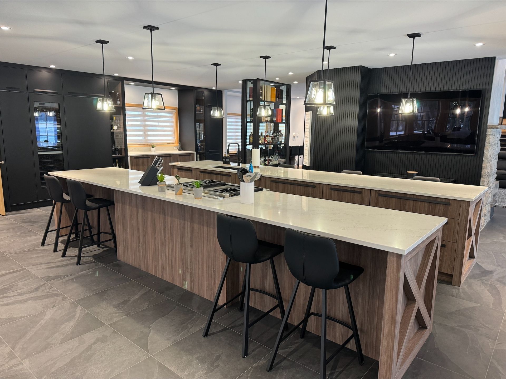 Cuisine moderne avec deux grands îlots, plans de travail en bois clair, placards noirs et luminaires suspendus.