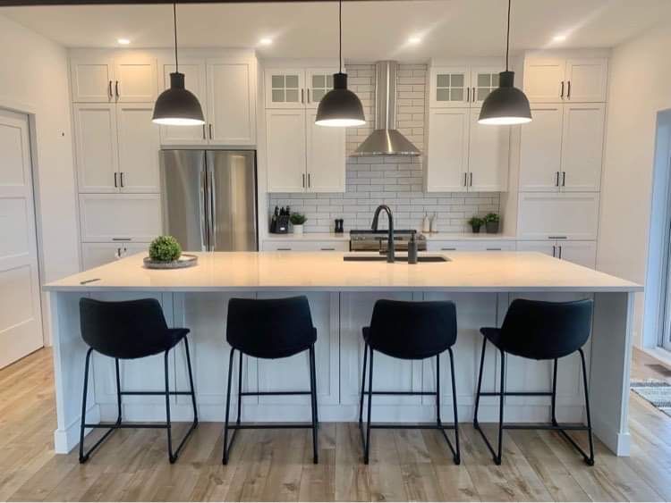 Cuisine blanche moderne avec îlot central, suspensions lumineuses noires et tabourets de bar noirs.