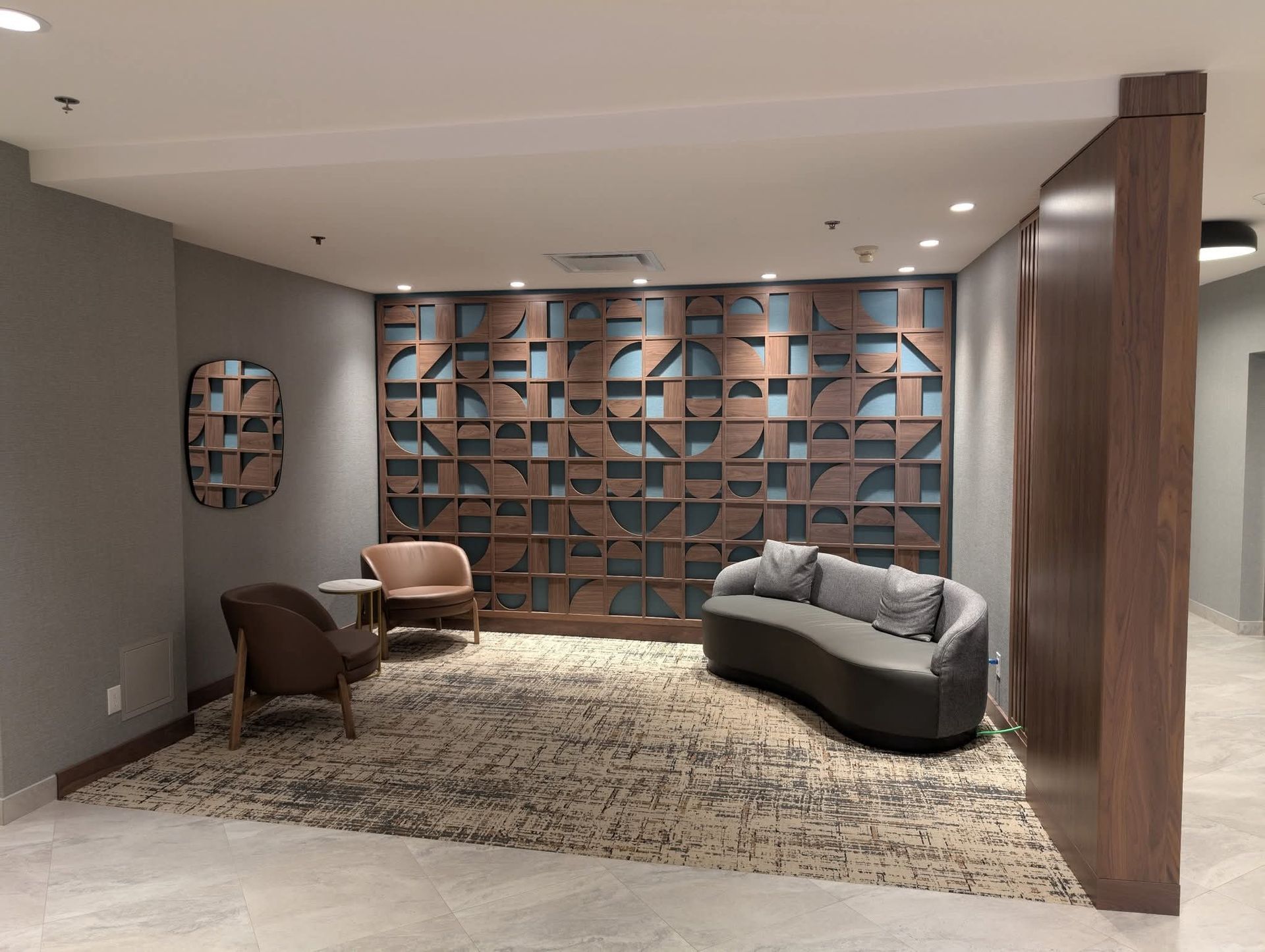 Coin salon avec murs gris, tapis à motifs, panneau mural décoratif en bois, sièges et table basse.