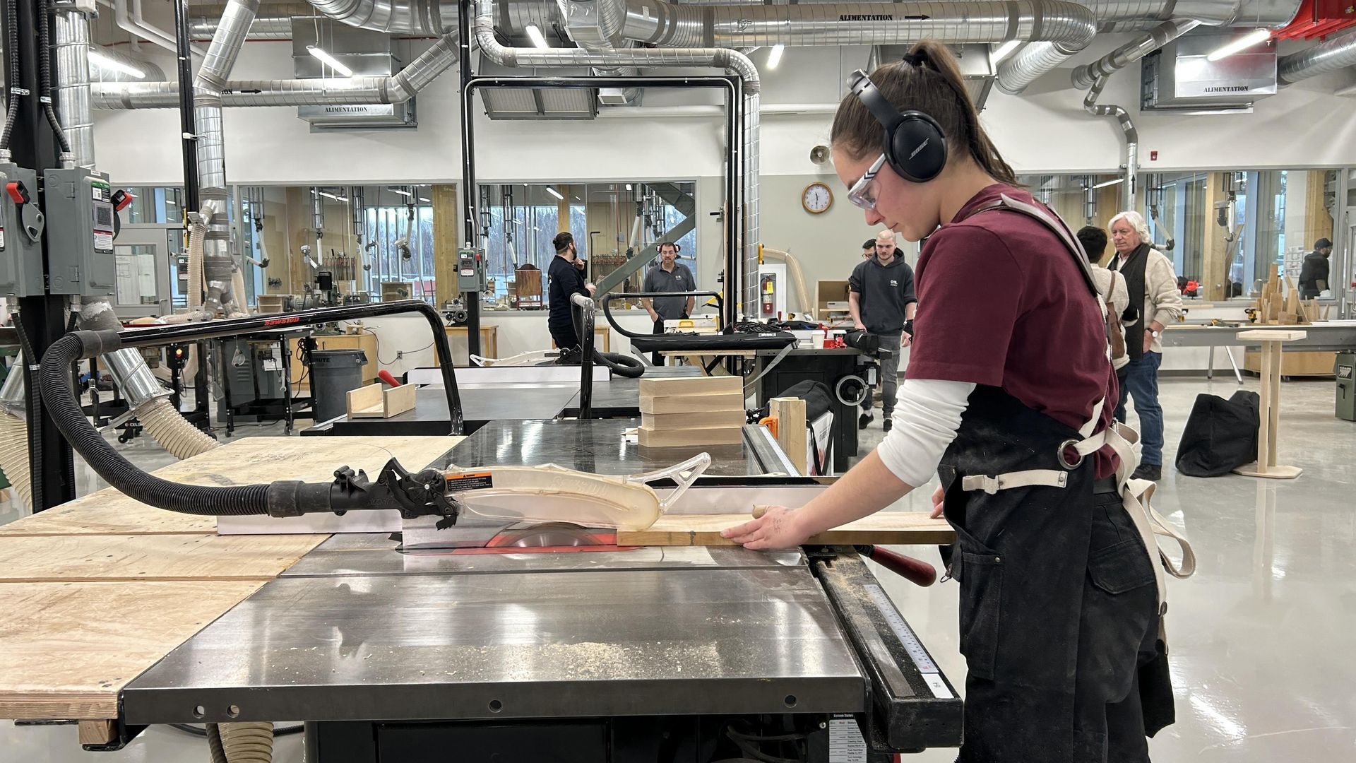 Femme utilisant une scie circulaire dans un atelier, portant des lunettes de sécurité et une protection auditive.