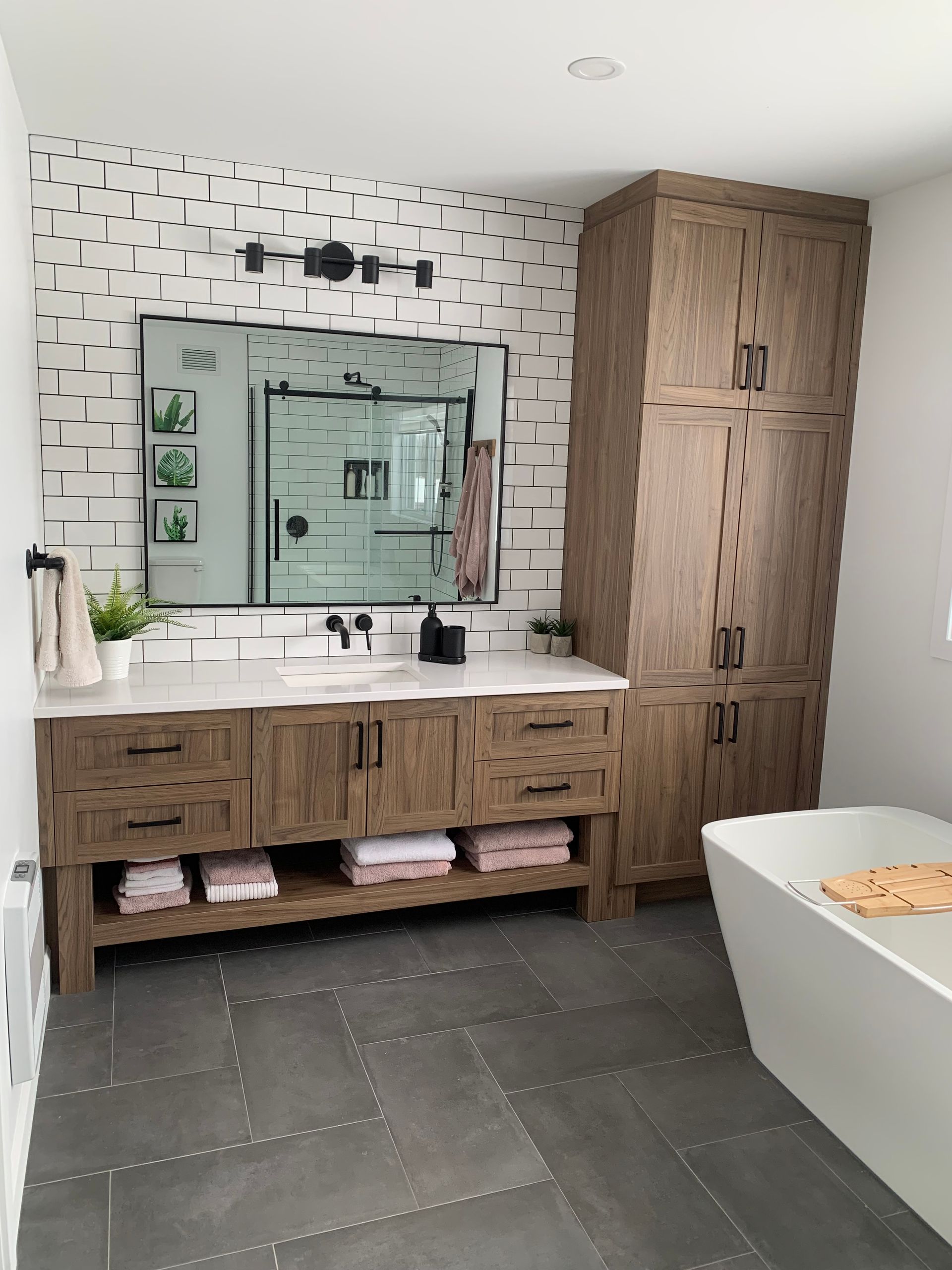 Salle de bains avec meuble-lavabo en bois, crédence à motifs, armoire haute et baignoire îlot. Sol carrelé gris.