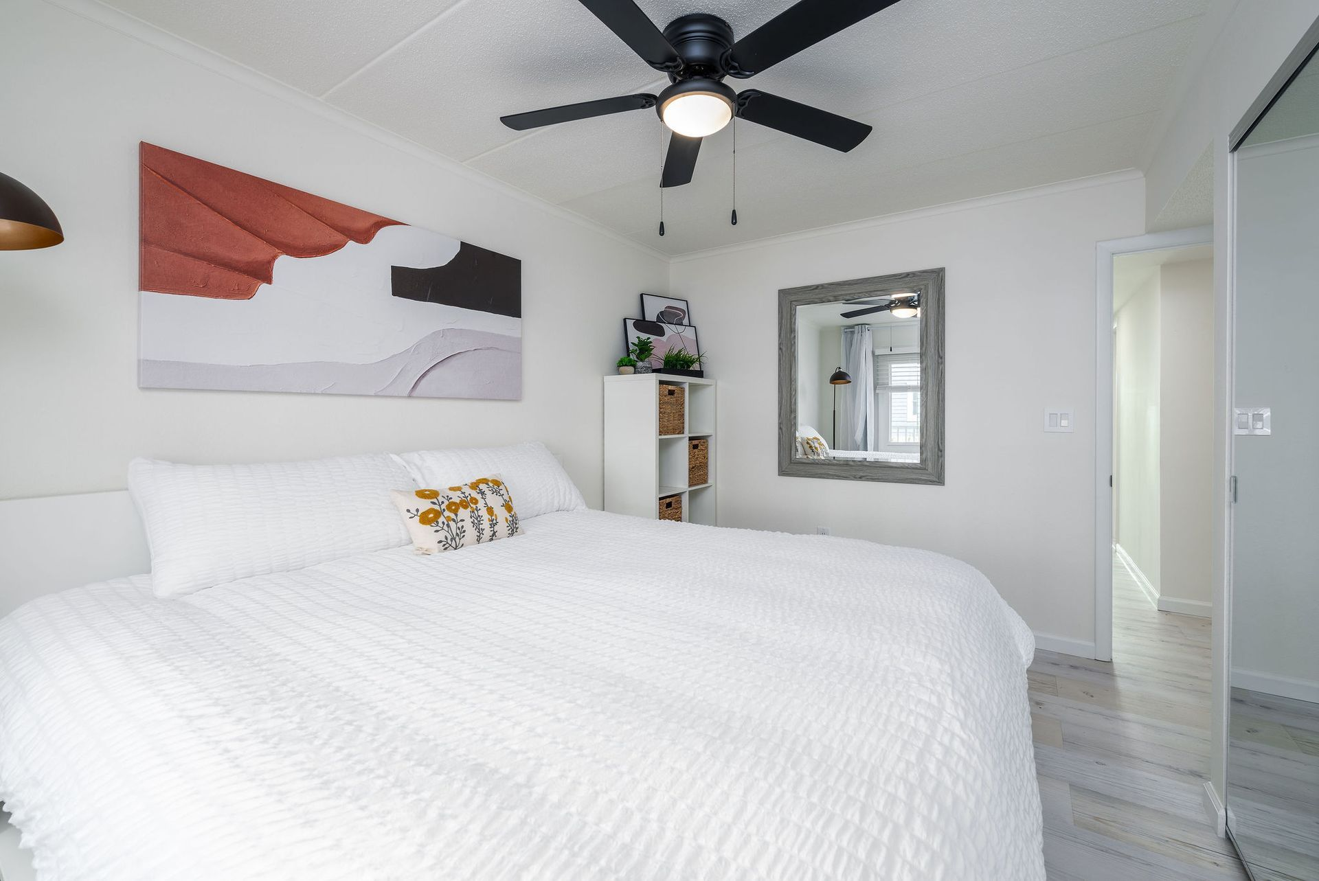 Bedroom with white bedding, artwork, ceiling fan, and a mirror.
