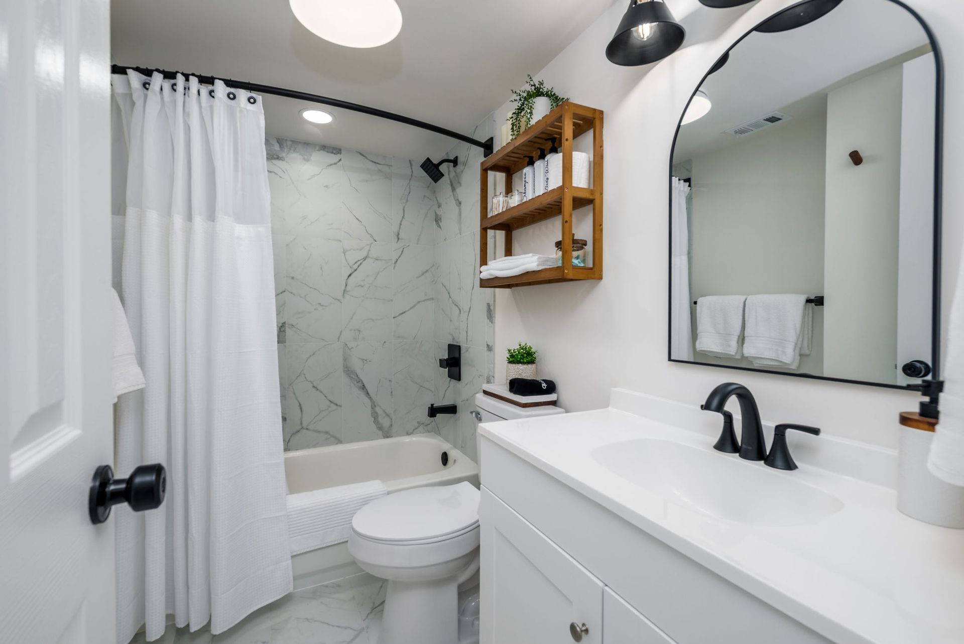 Bathroom with white walls, marble shower, white vanity, black fixtures, and mirror.