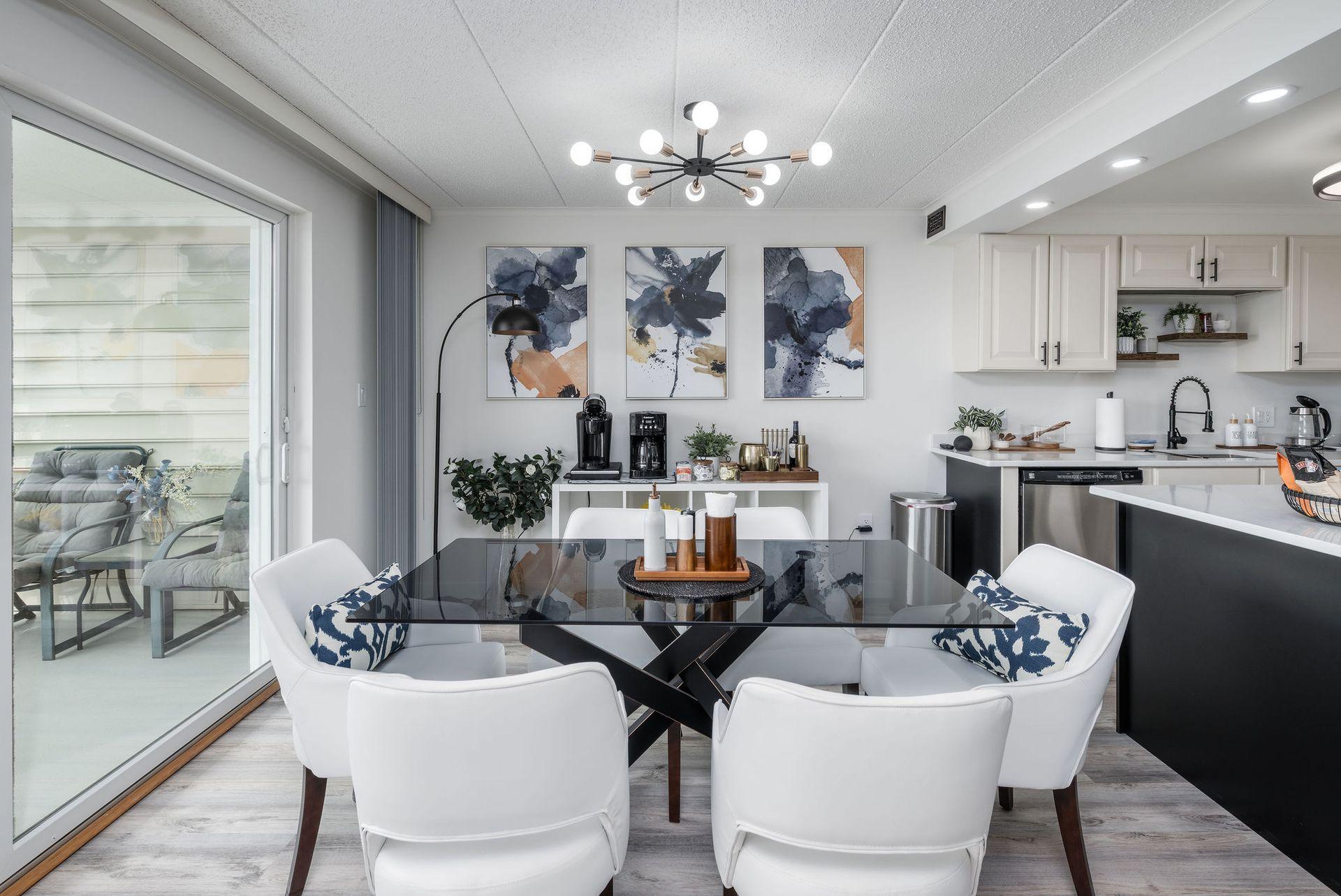 Dining area with a black table and white chairs, adjacent to a kitchen with white cabinets.