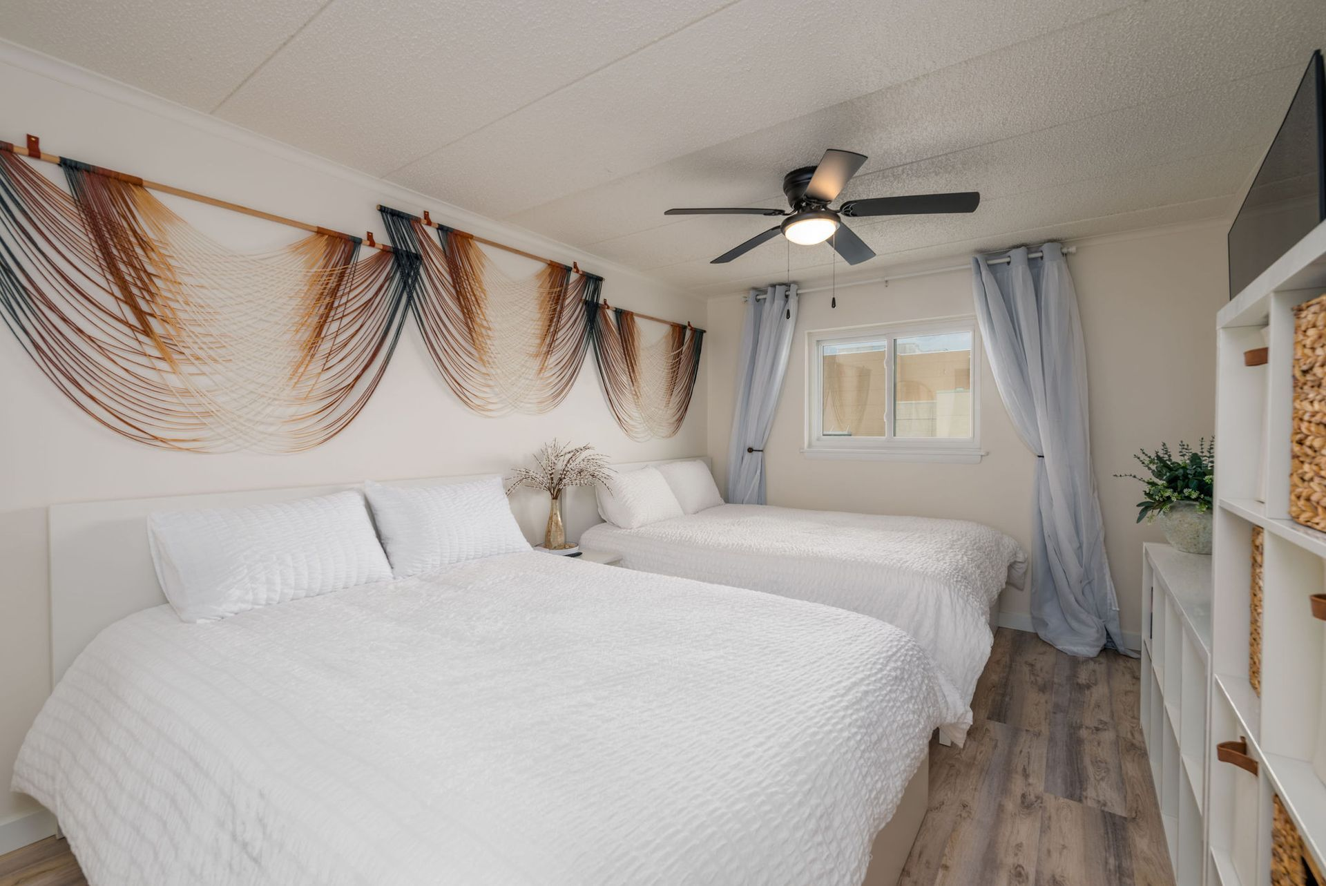 Bedroom with two white beds, blue curtains, and woven wall art.