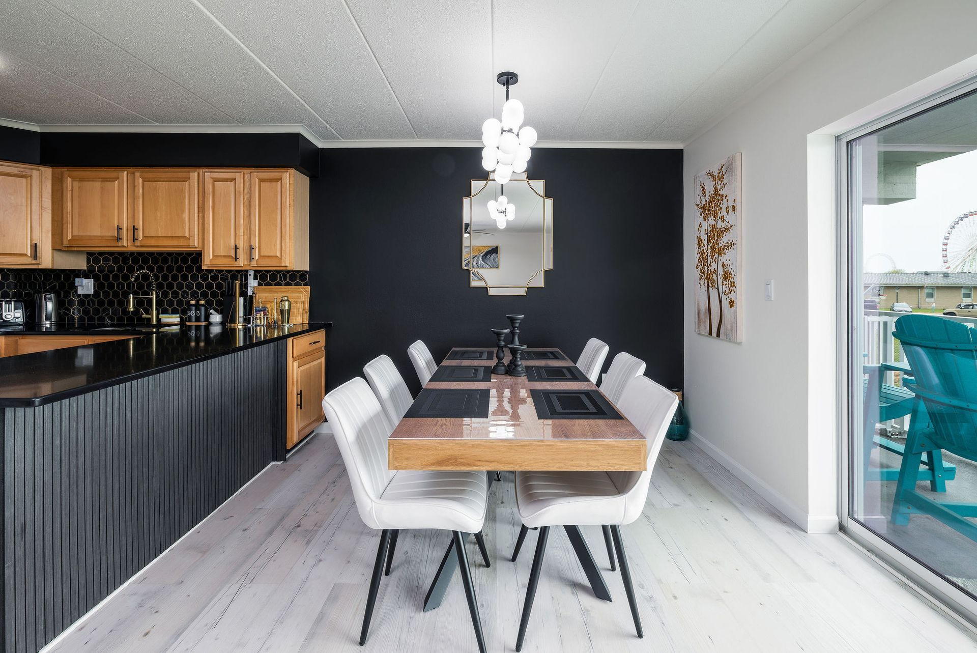 Dining area with a black accent wall, wooden table, and white chairs. Kitchen with black countertops is visible.