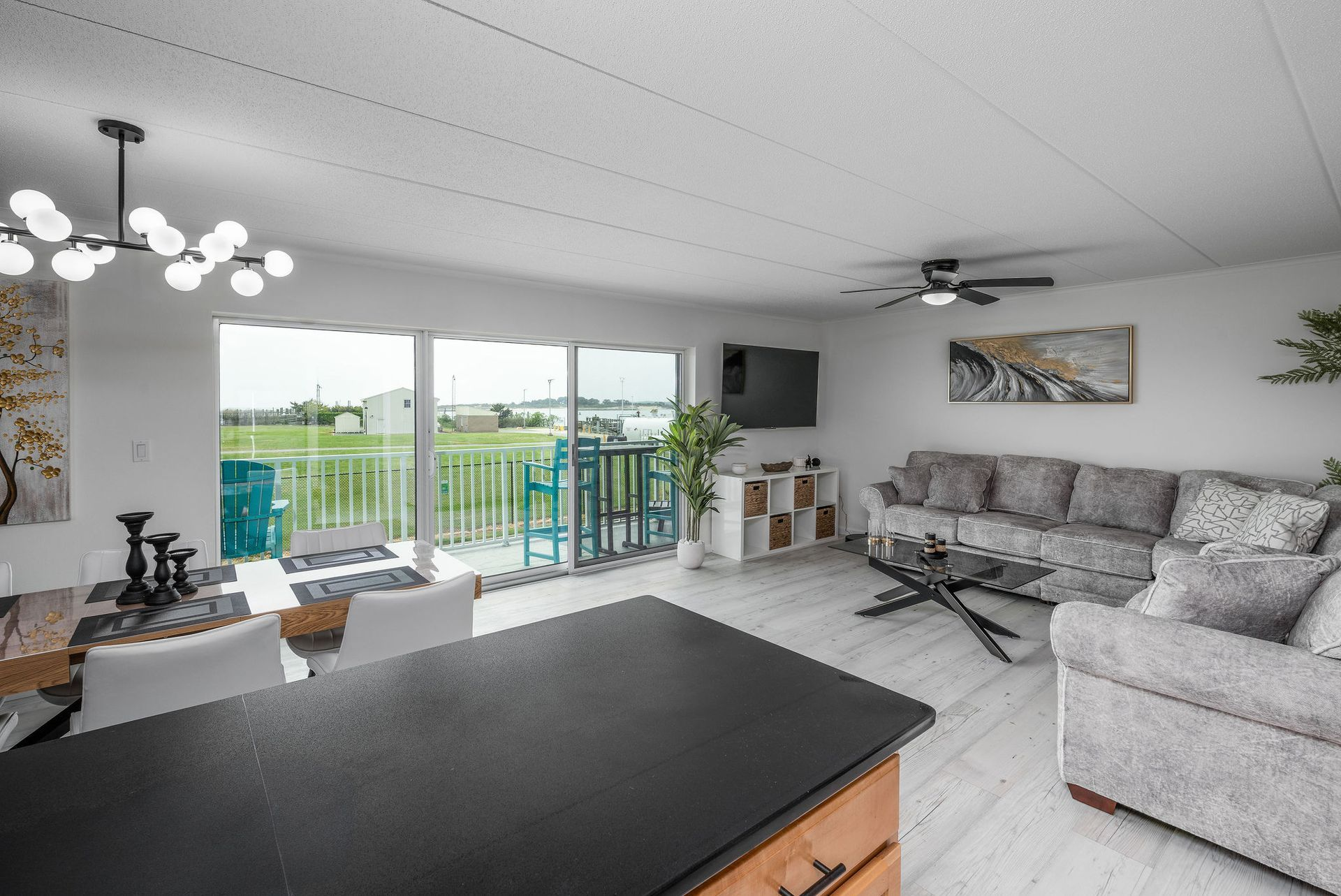 Living room with a view: white walls, sofa, TV, glass table, and balcony overlooking greenery.