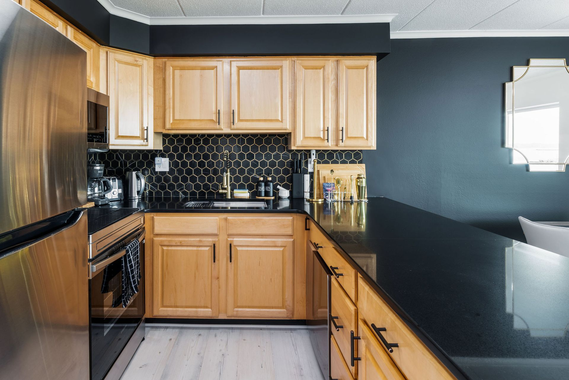 Kitchen with light wood cabinets, black countertops, and dark blue walls.