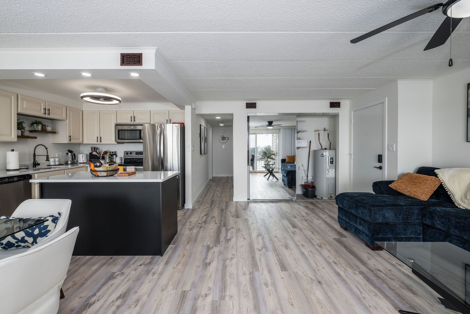 Open-concept apartment with kitchen, living area, and hallway. Gray and white color scheme, wood-look flooring.