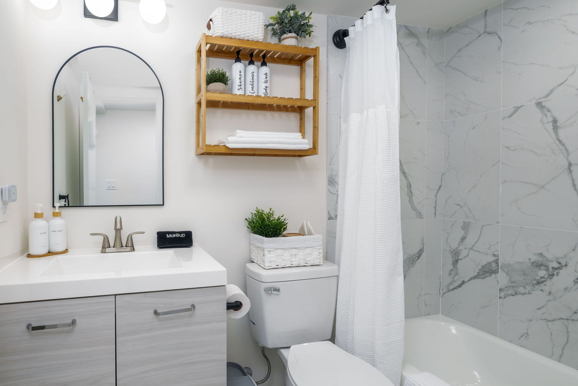 Small, modern bathroom with white and gray marble tiles, wood shelving, and a vanity.