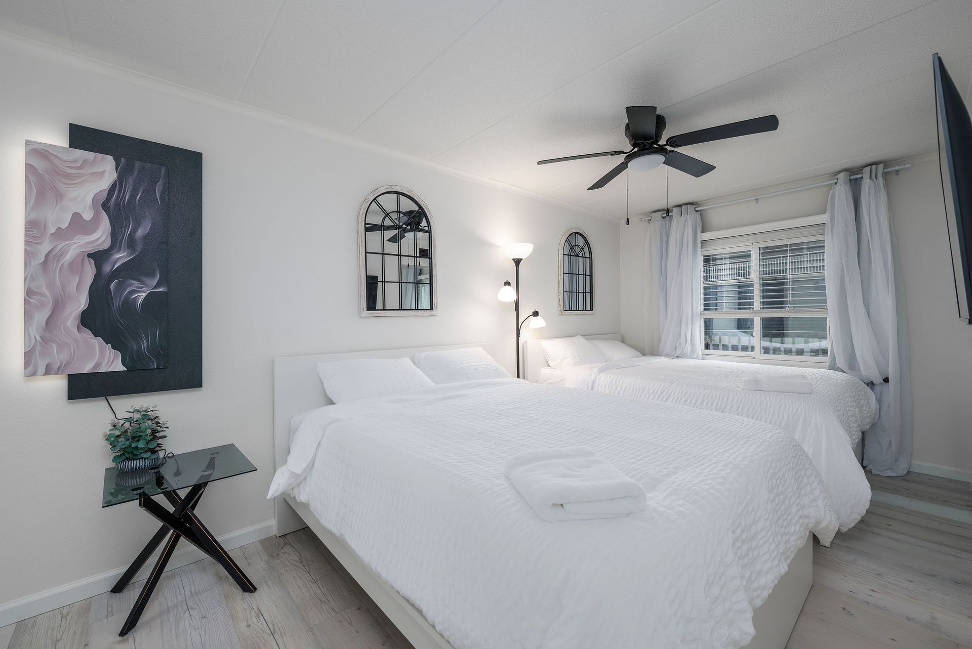 Bedroom with two white beds, artwork, and a ceiling fan.