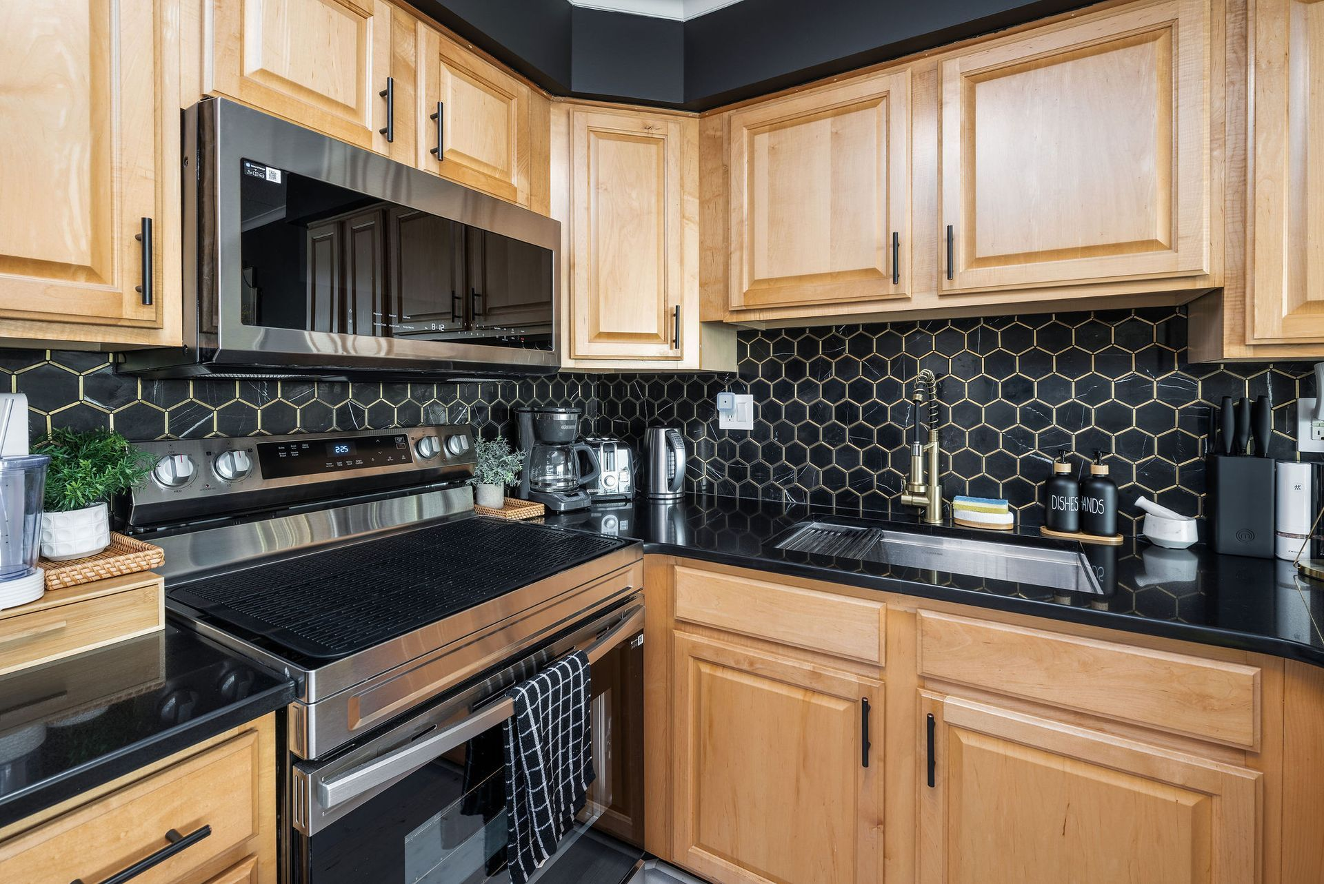 A kitchen with light wood cabinets, black countertops, and a black honeycomb backsplash.