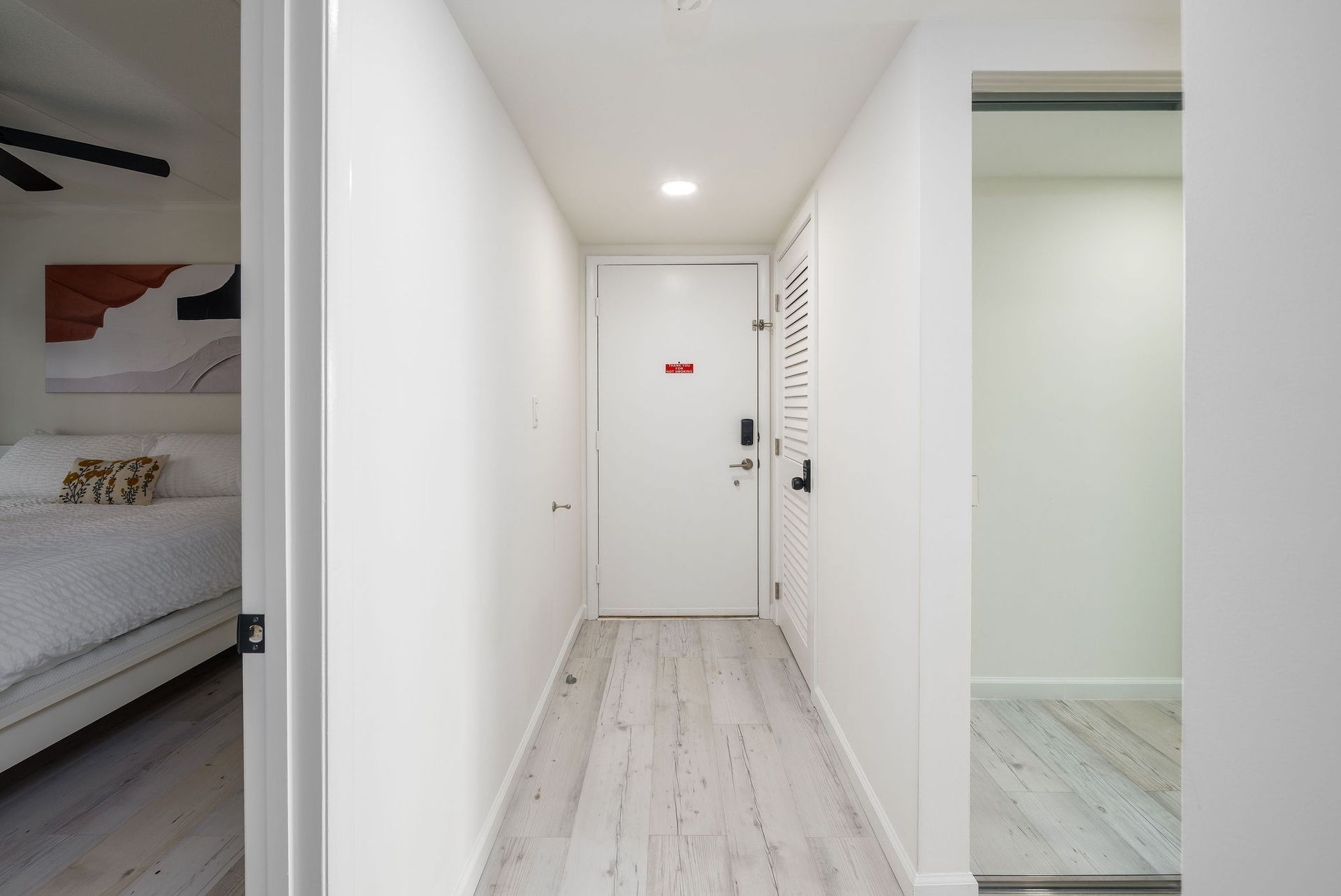 Long hallway with white walls and a light wood floor leading to a closed white door.
