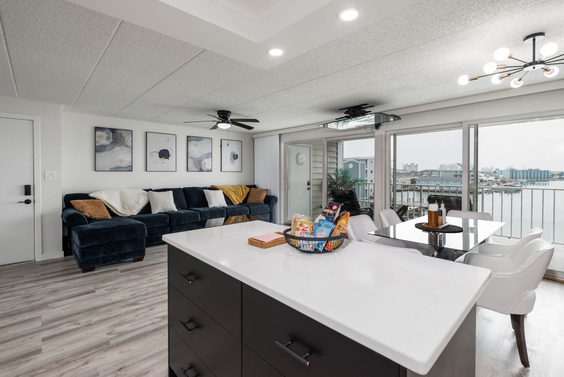 Open-concept condo with a kitchen island, living room with a dark blue sofa, and dining area with water views.