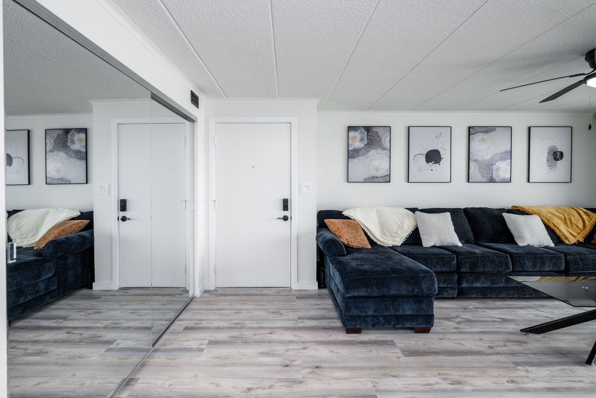 Living room with dark blue sectional sofa, artwork on white walls, mirrored wall, and light wood flooring.