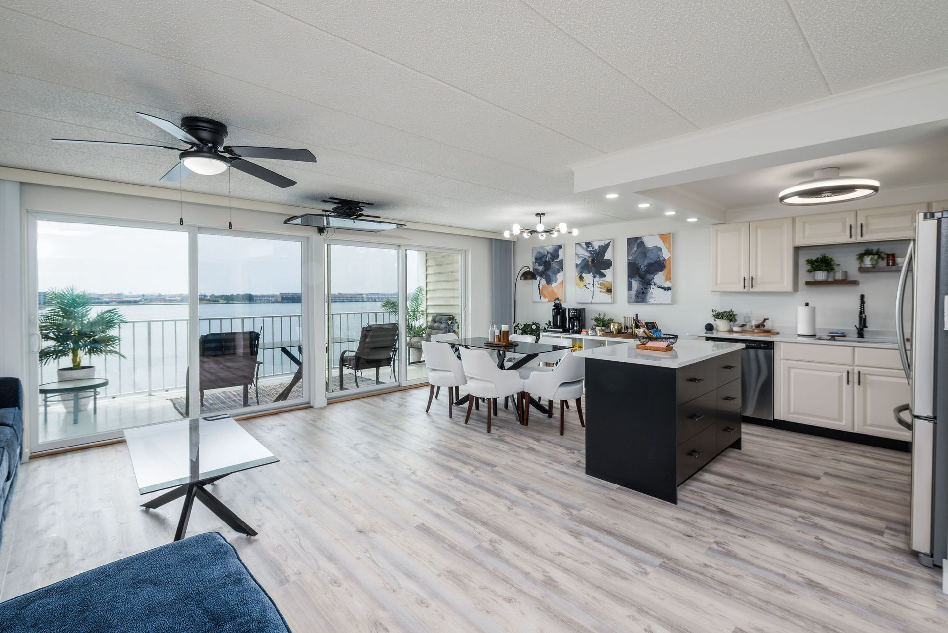 Modern open-plan living space with a kitchen, dining area, and balcony overlooking water.