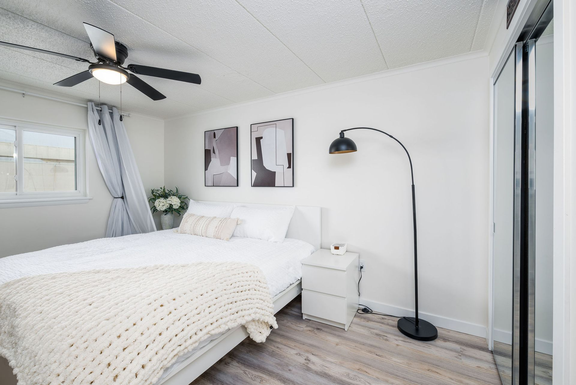 Bedroom with a white bed, neutral decor, artwork, and a black arc lamp.