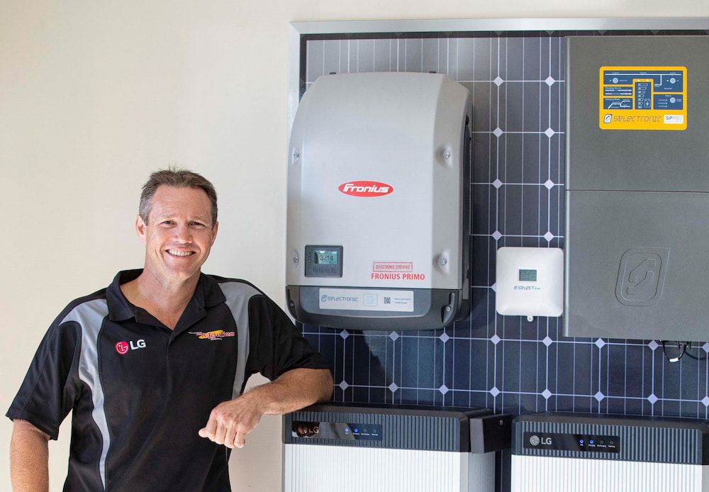 Man Poses With Solar Panel Equipment, Including An Inverter, Battery Storage Units — Mackies in Port Macquarie, NSW