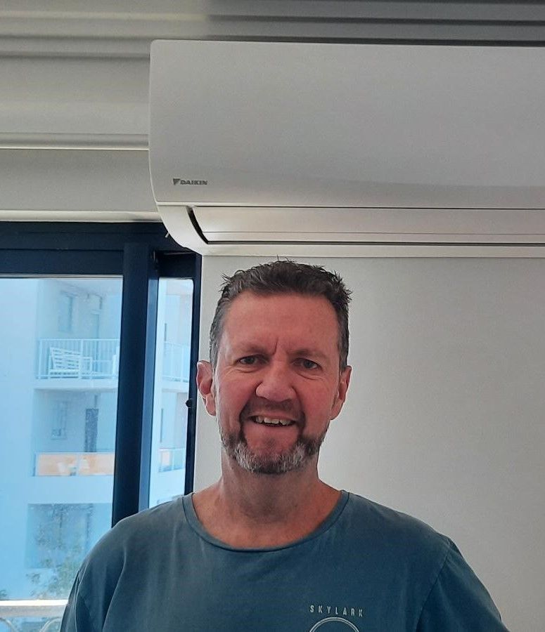 Man Smiling In Front Of A White Air Conditioning Unit — Mackies in Taree, NSW