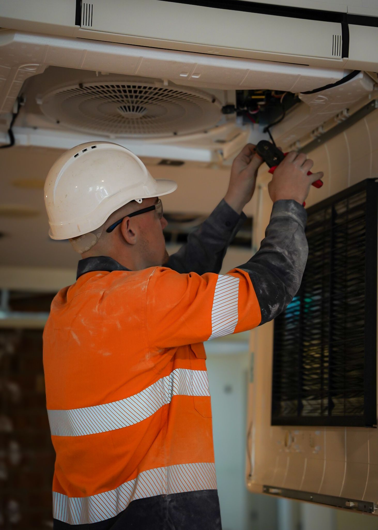 Construction Worker In Orange Safety Gear And Hard Hat Working On Ceiling Fixture — Mackies in Taree, NSW