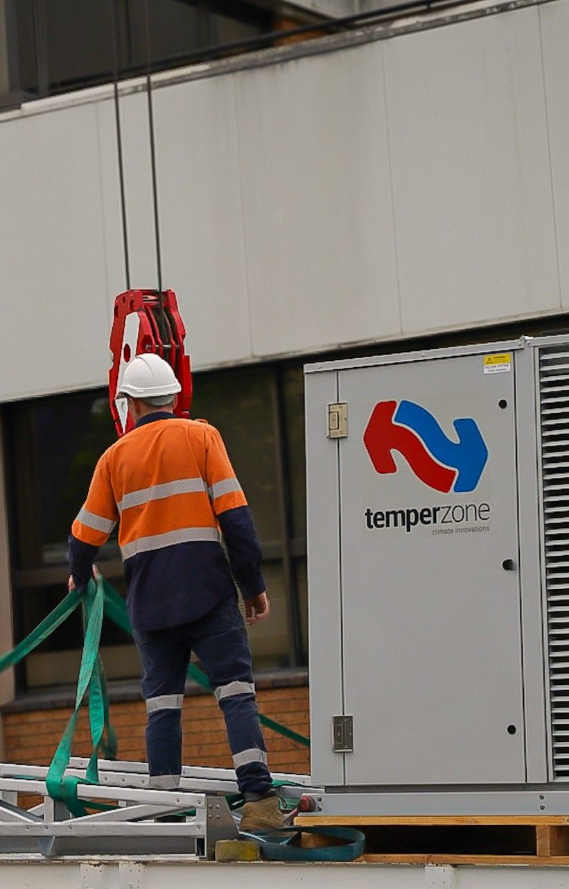 Construction Worker In Safety Gear Guiding The Lift Of A Temperzone Hvac Unit Onto A Building Roof — Mackies in Taree, NSW