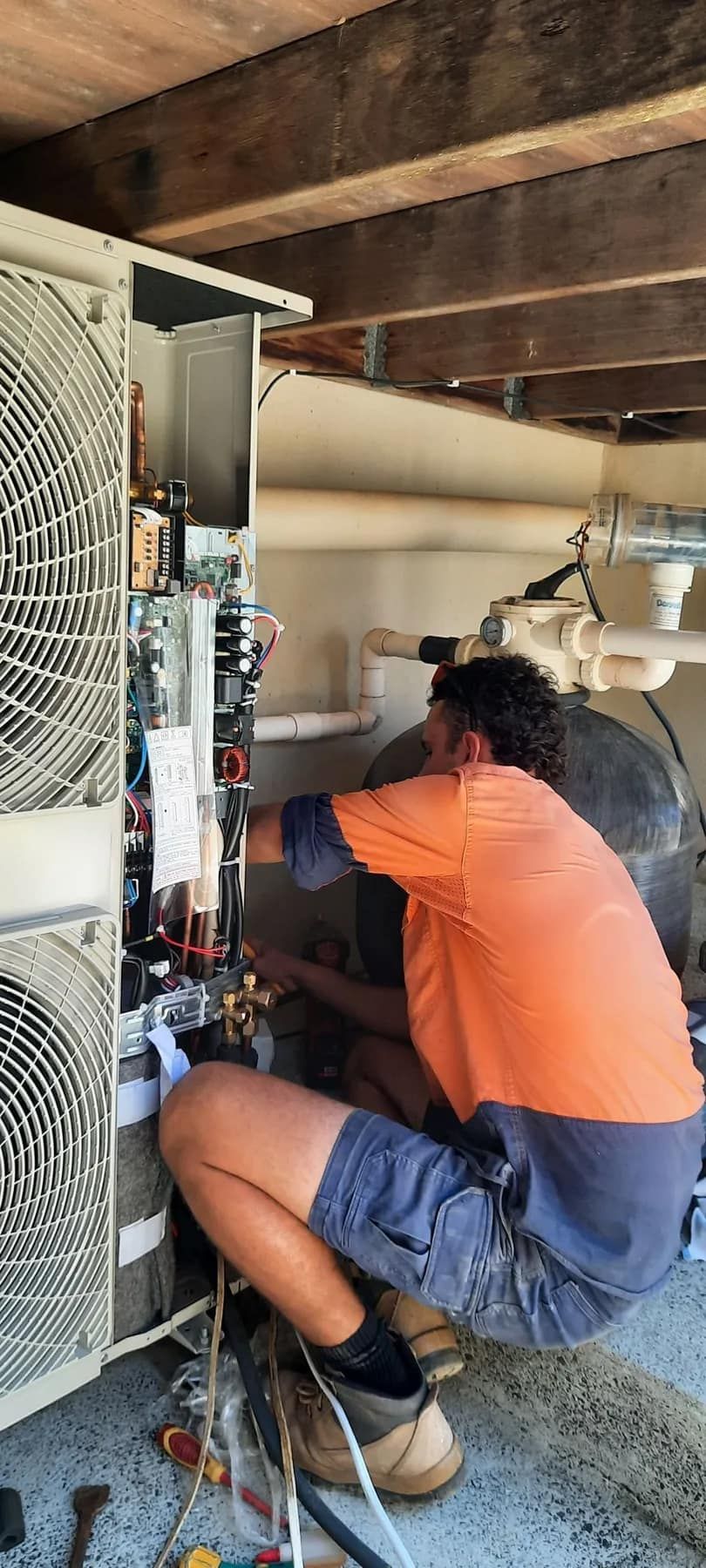 A Worker In An Orange Shirt And Blue Shorts Crouches — Mackies in Taree, NSW