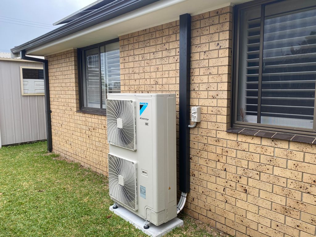 Outdoor Air Conditioning Unit Mounted On A Brick Wall Next To A Window And Vent — Mackies in Taree, NSW