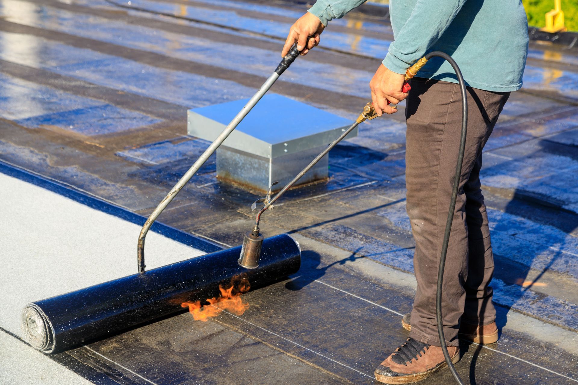Worker torching a rolled roofing membrane on a flat roof during installation