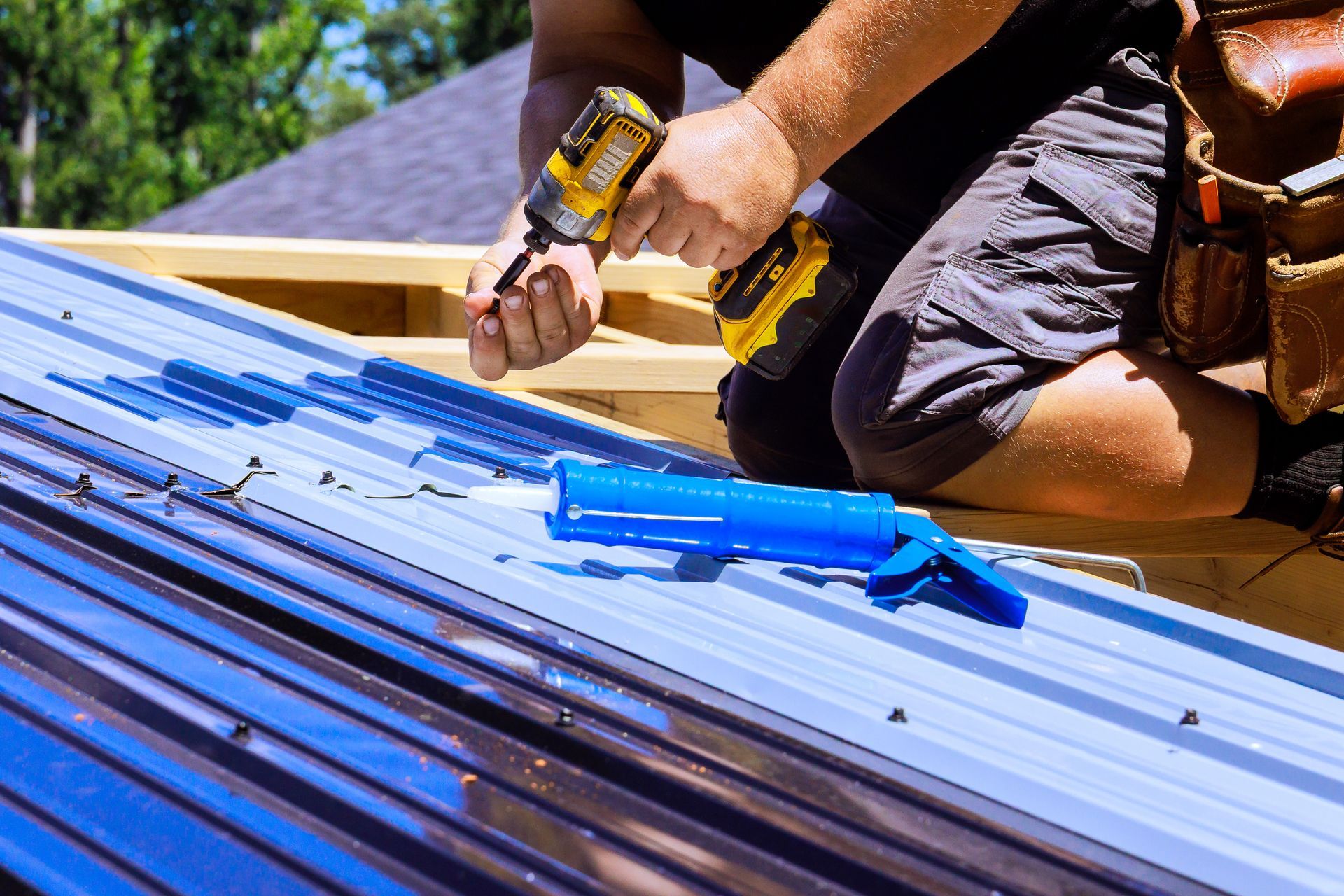 Person using a drill to fasten blue roofing panels on a roof under construction Person using a drill to fasten blue roofing panels on a roof under construction