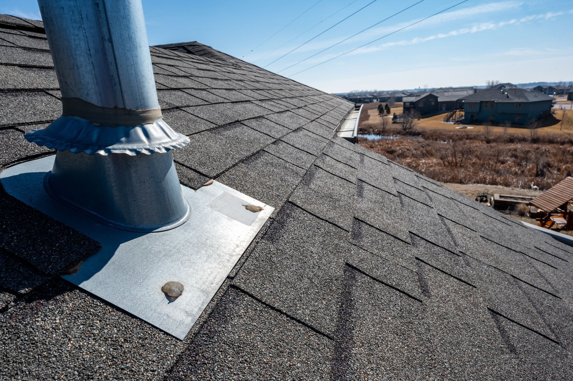 Roof vent pipe on gray asphalt shingles with a chimney cap, under a clear blue sky Roof vent pipe on gray asphalt shingles with a chimney cap, under a clear blue sky