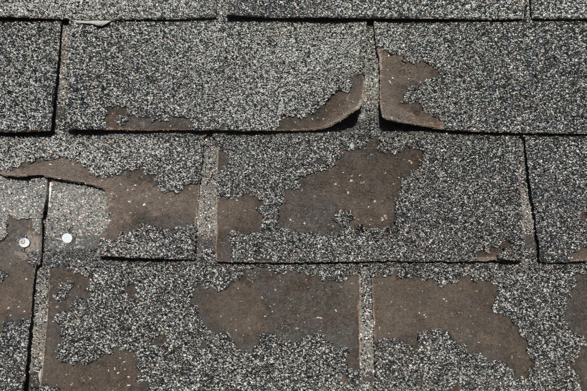 Damaged asphalt shingles on a roof with large peeling patches and exposed underlayment