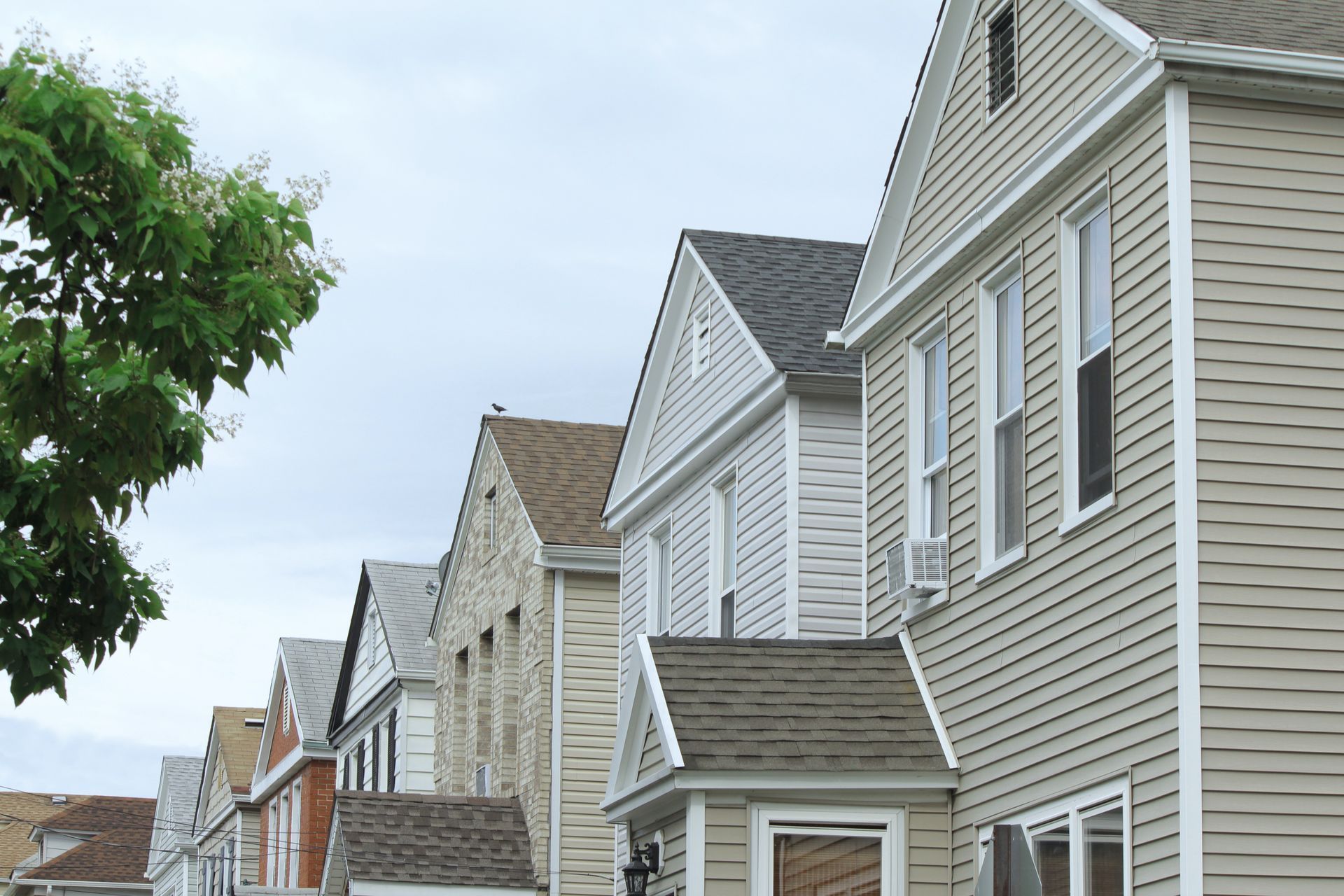 Row of closely packed suburban houses with gray siding under a cloudy sky