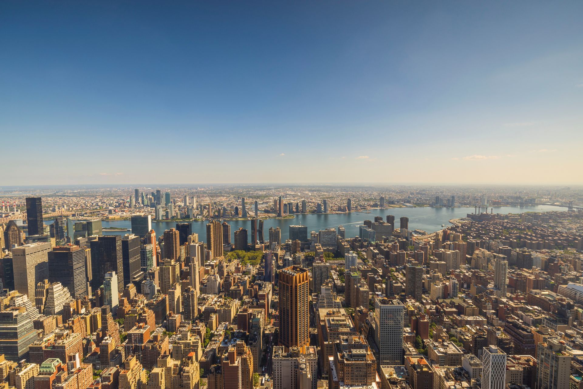 Aerial view of a sprawling city skyline with tall skyscrapers beside a river at sunset