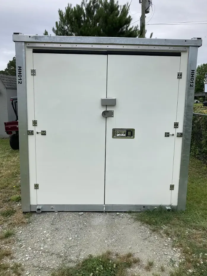 White double-door storage container with metal frame; gray gravel ground.