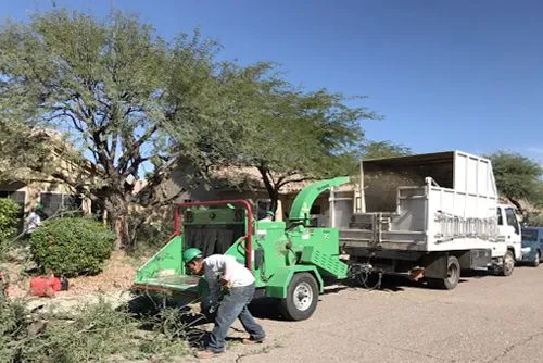 A man is working on a tree chipper next to a truck.