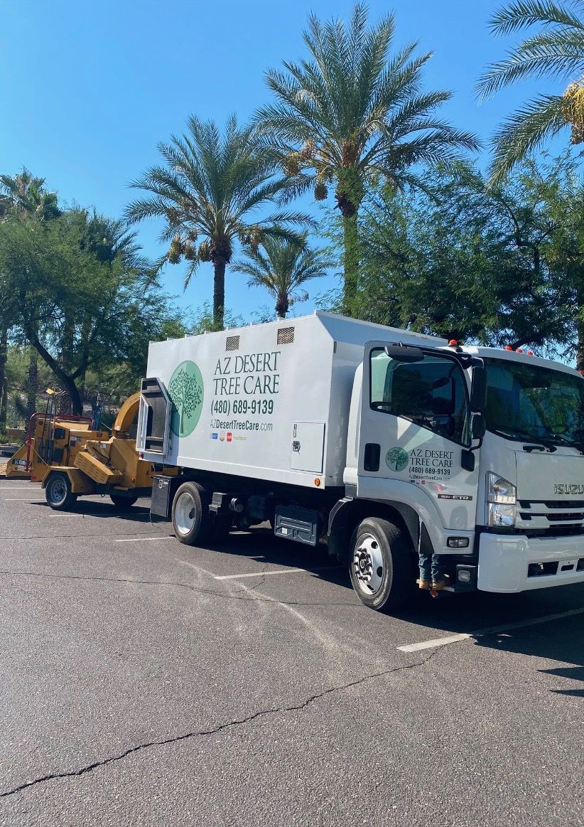 A white tree service truck parked in a sunny lot with a yellow wood chipper attached to the back.