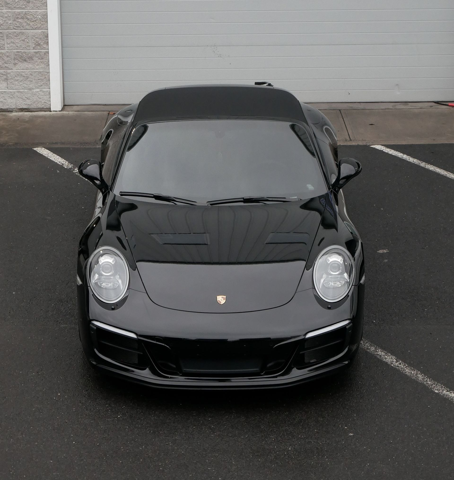 Black Porsche sports car parked in a lot, front view against a gray garage door.