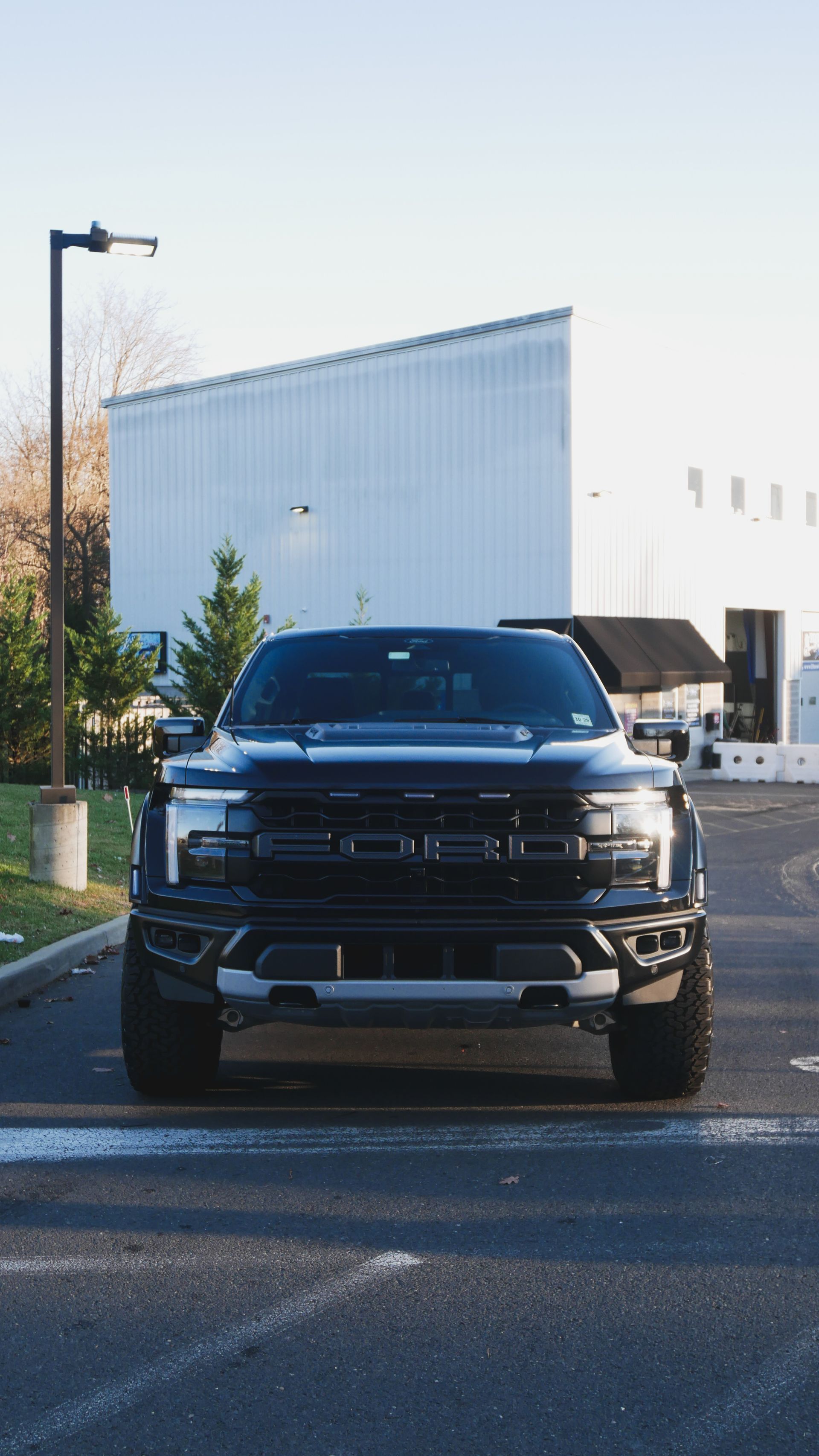 Front view of a black pickup truck parked on a street beside a white industrial building.