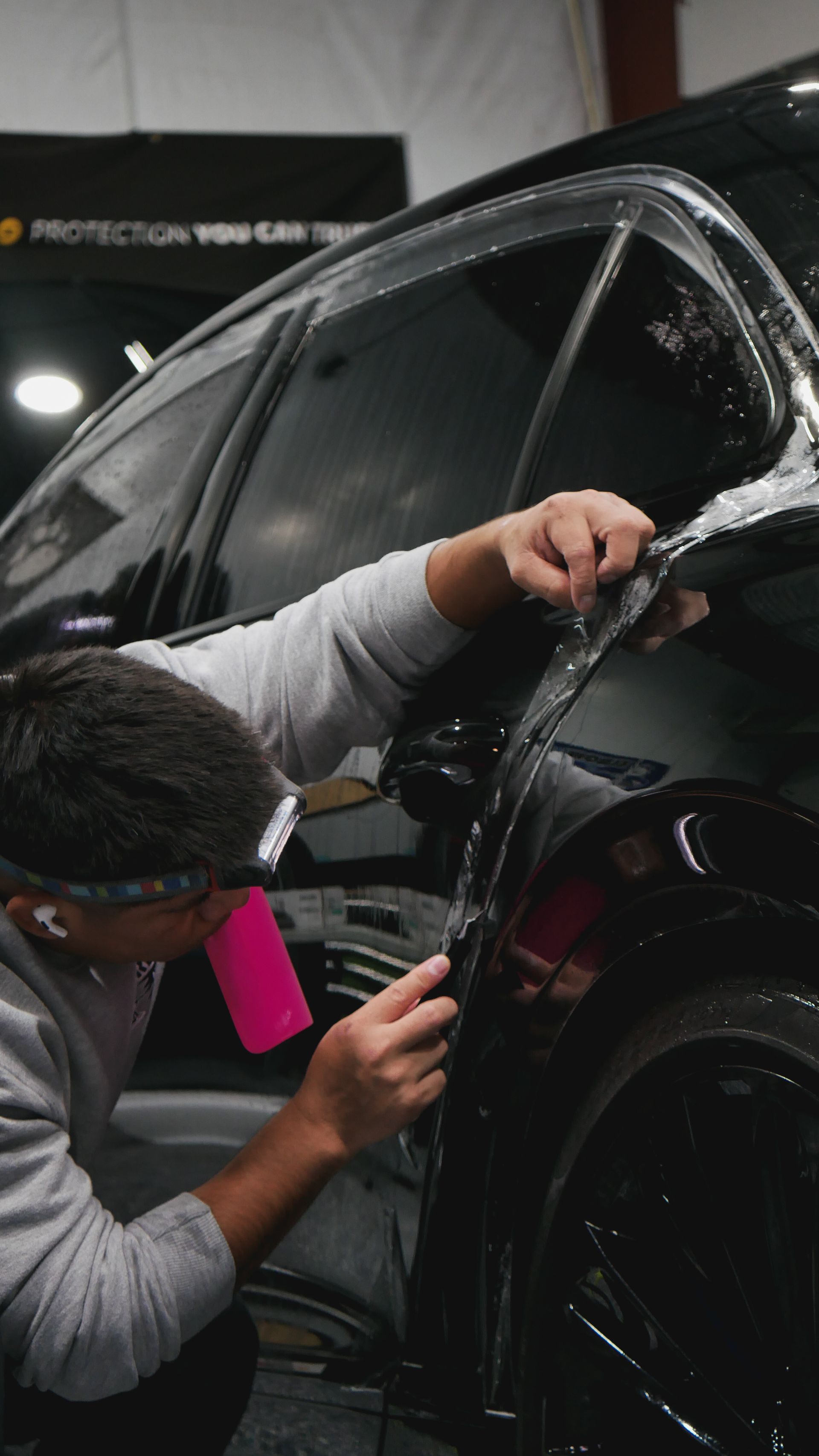 Person applying window tint to a black car in a workshop